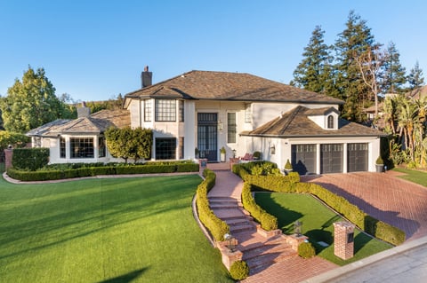 A luxury estate with a manicured lawn, brick driveway, grand entrance, and elegant architectural design