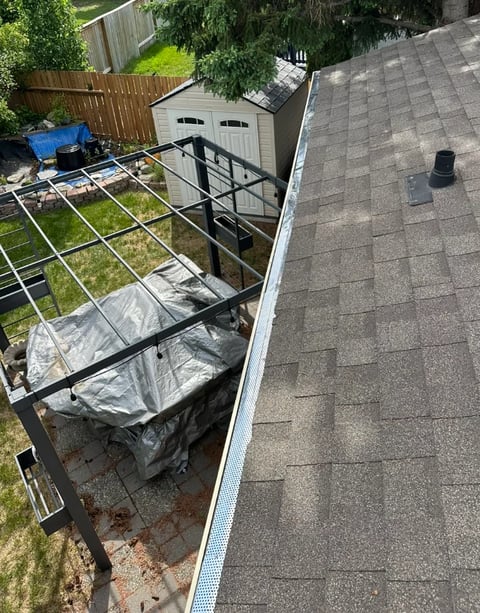 Overhead view of a backyard with a covered patio area, white garage, wooden fence, and green lawn