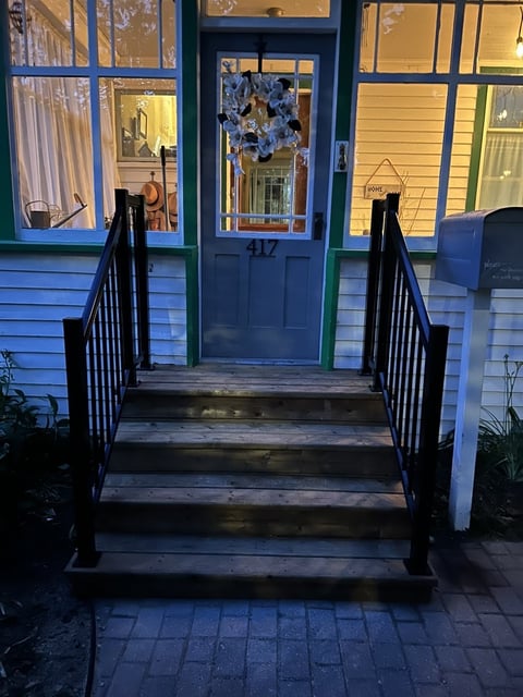 Front entrance of a house with blue door numbered 417, black metal railings on wooden steps, and lit windows at dusk