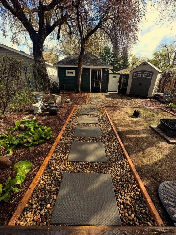 Backyard with pea gravel pathway leading to storage sheds under large trees